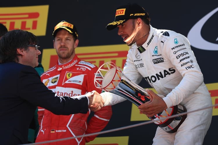 Lewis Hamilton accepts a first-place trophy whilst a disappointed Sebastian Vettel looks on