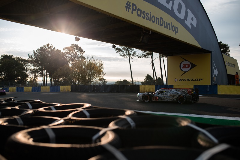 The #1 Rebellion Racing LMP1 car driving through Dunlop at the 2020 24 Hours of Le Mans at sunrise